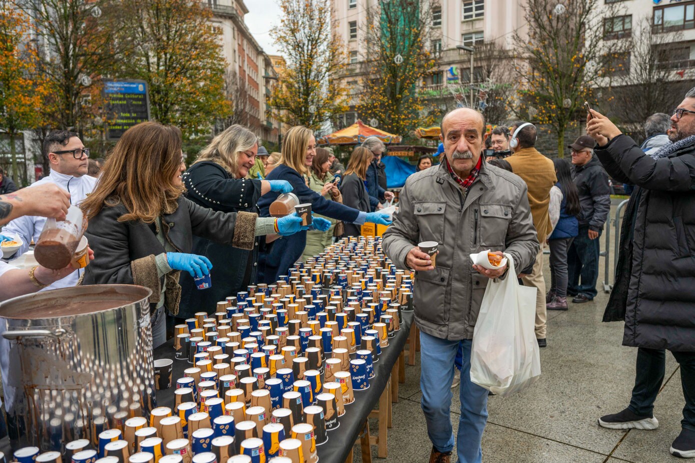 Un hombre avanza en la fila mientras las voluntarias reparten el dulce con guantes azules. 